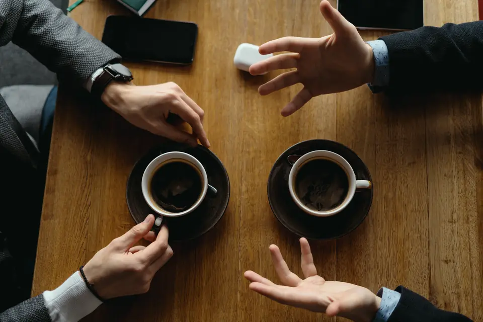 Mãos conversando sobre a mesa de madeira, entre xícaras de café.