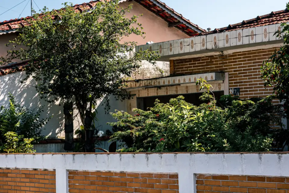 Casa de tijolinho atrás do muro, com árvore e jardim na frente.