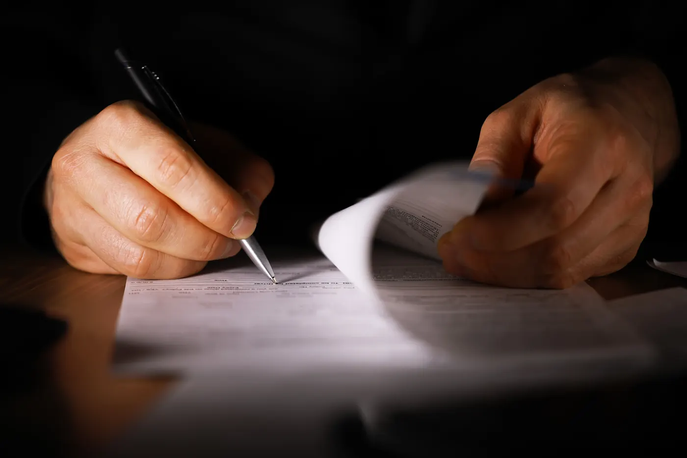 Mão assinando um contrato sob luz baixa.