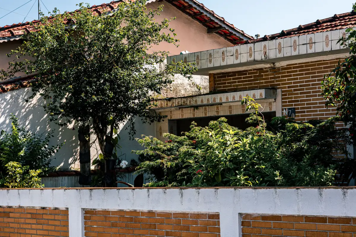 Casa de tijolinho atrás do muro, com árvore e jardim na frente.