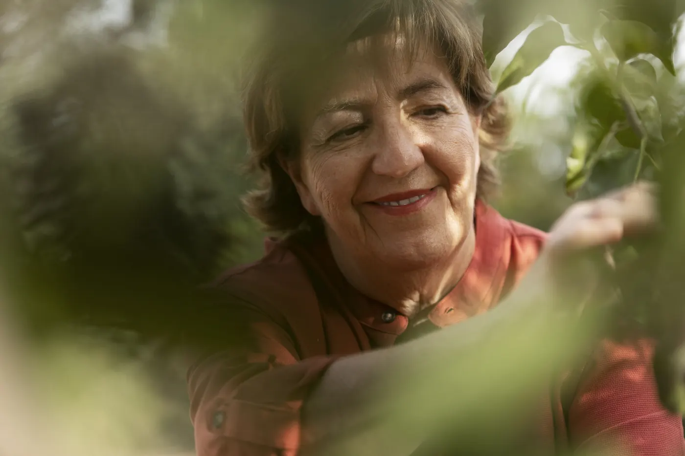 Senhora sorrindo entre as plantas do quintal.
